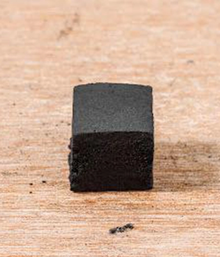 Single charcoal cube on a wooden surface showcasing precise shape and premium quality for controlled burns